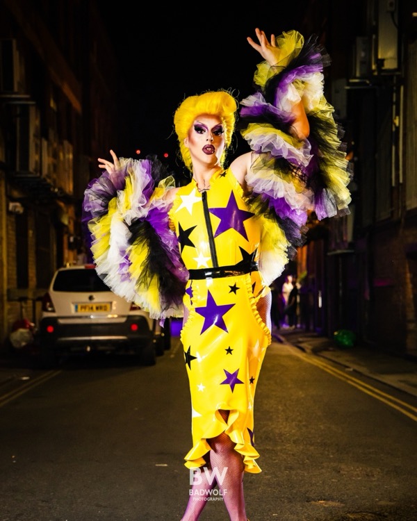 Letitia Delish in a star-print latex outfit with ruffled sleeves, posing on a city street at night